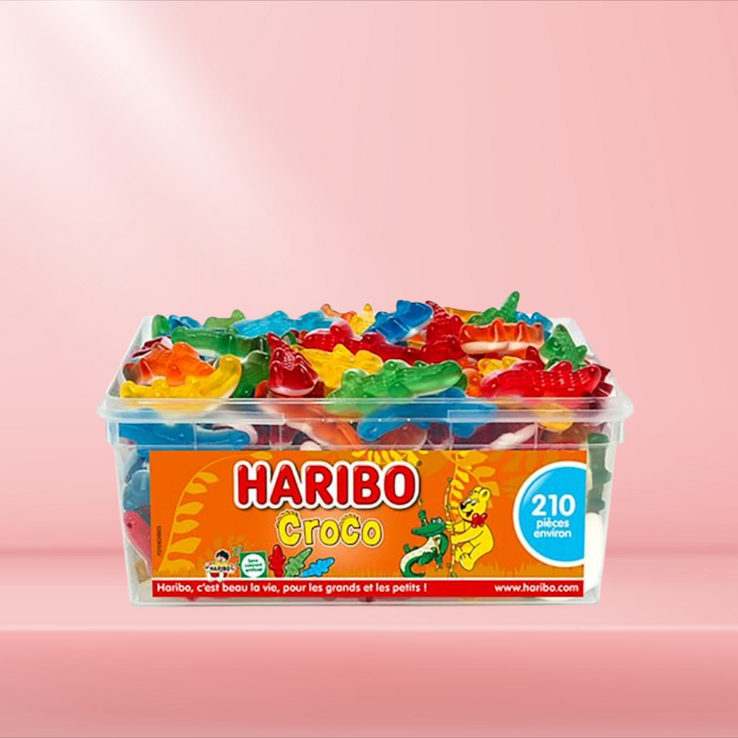 Boîte de bonbons Haribo Croco, assortiments de crocodiles gélifiés colorés, sur fond rose.