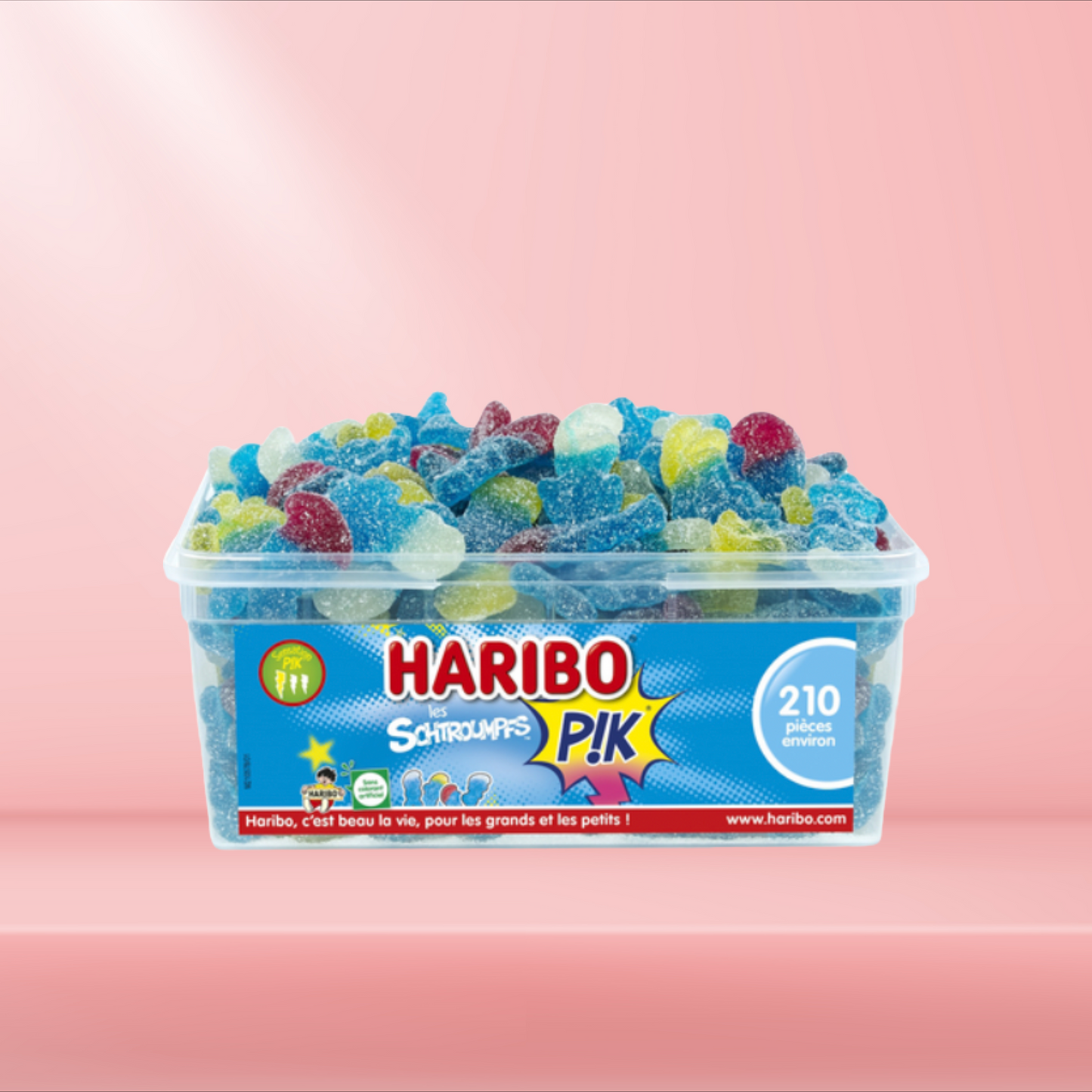 Boîte de bonbons Haribo Schtroumpfs Pik, bonbons gélifiés acidulés en forme de Schtroumpfs, sur fond rose.