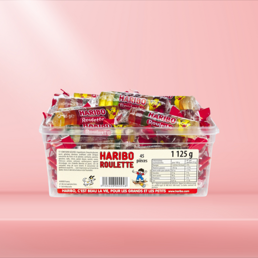 Boîte de bonbons Haribo Roulette, rouleaux de bonbons gélifiés aux saveurs fruitées, sur fond rose.