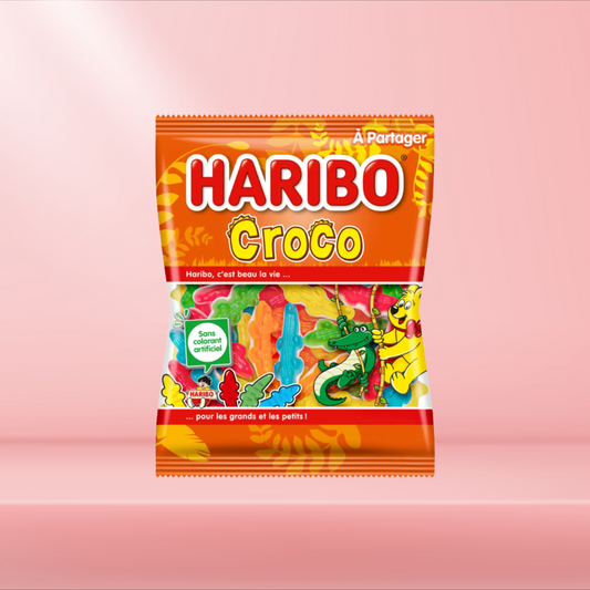 Sachet de bonbons Haribo Croco, bonbons gélifiés en forme de crocodiles aux saveurs fruitées, sur fond rose.